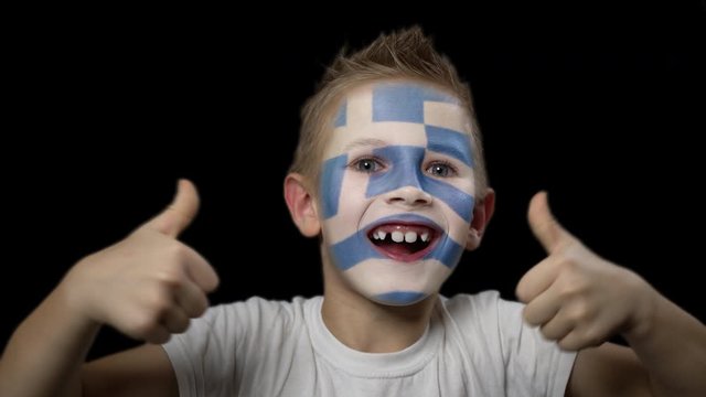 Happy boy rejoices victory of his favorite team of Greece. A child with a face painted in national colors. Portrait of a happy young fan. Joyful emotions and gestures. Victory. Triumph.