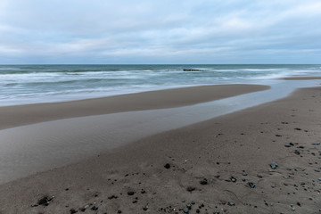 landscape of wide sandy beach by the cold Baltic sea in cloudy weather at long exposure