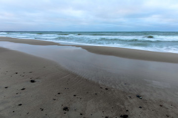 landscape of wide sandy beach by the cold Baltic sea in cloudy weather at long exposure