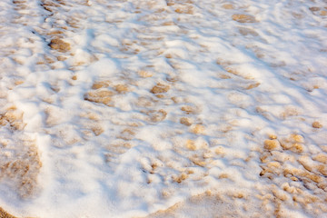 sea waves splash foam on the sunny beach.  mess of salt water and sand in evening light. dynamic nature texture