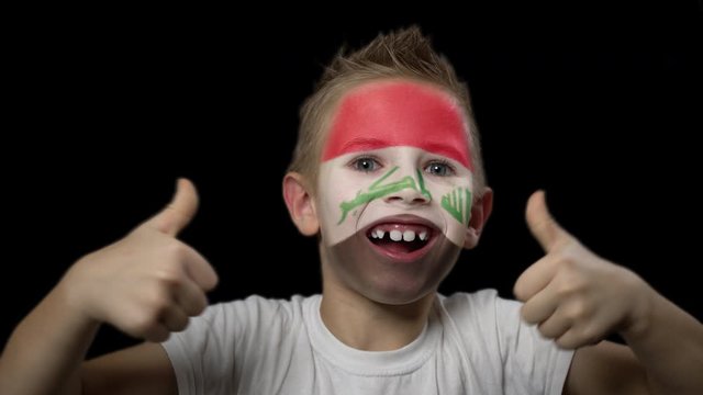 Happy boy rejoices victory of his favorite team of Iraq. A child with a face painted in national colors. Portrait of a happy young fan. Joyful emotions and gestures. Victory. Triumph.