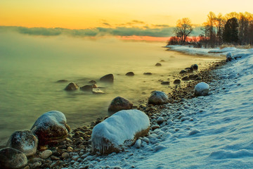 Large stones in an unfrozen lake in winter with evaporation from the water at sunset.
