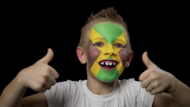 Happy boy rejoices victory of his favorite team of Jamaica. A child with a face painted in national colors. Portrait of a happy young fan. Joyful emotions and gestures. Victory. Triumph.