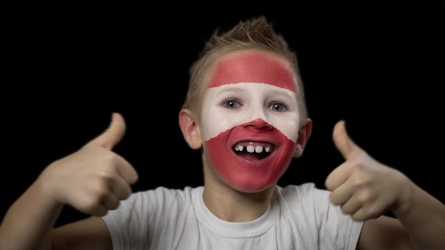 Happy boy rejoices victory of his favorite team of Latvia. A child with a face painted in national colors. Portrait of a happy young fan. Joyful emotions and gestures. Victory. Triumph.