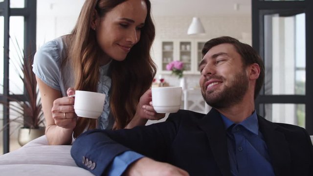 Smiling couple drinking tea at home together. Joyful couple taking coffee break