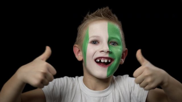 Happy boy rejoices victory of his favorite team of Nigeria. A child with a face painted in national colors. Portrait of a happy young fan. Joyful emotions and gestures. Victory. Triumph.