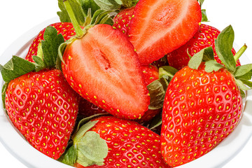 Ripe red strawberries with green leaves and two half of cutted strawberry on the foreground in a white bowl isolated on white background close-up