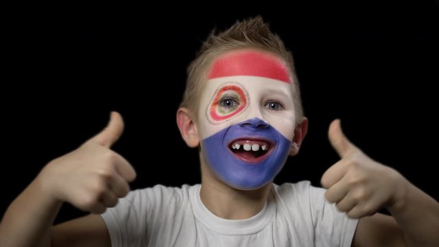 Happy boy rejoices victory of his favorite team of Paraguay. A child with a face painted in national colors. Portrait of a happy young fan. Joyful emotions and gestures. Victory. Triumph.