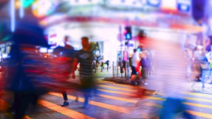 Pedestrians going on crosswalk in Hong Kong in evening. Buildings and skyscrapers illuminated at night. Busy life of asian metropolis with traffic. Tilt shift lens and blur effect. Time lapse