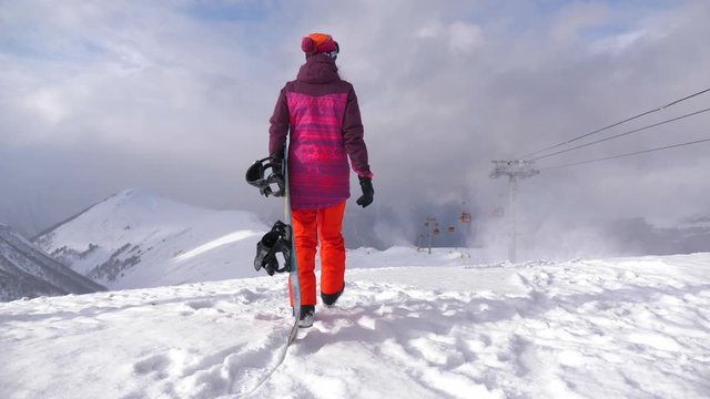 Girl with snowboard sitting on top and enjoying mountain landscape. Sport woman in snowy mountains. Beautiful amazing day winter mountains.