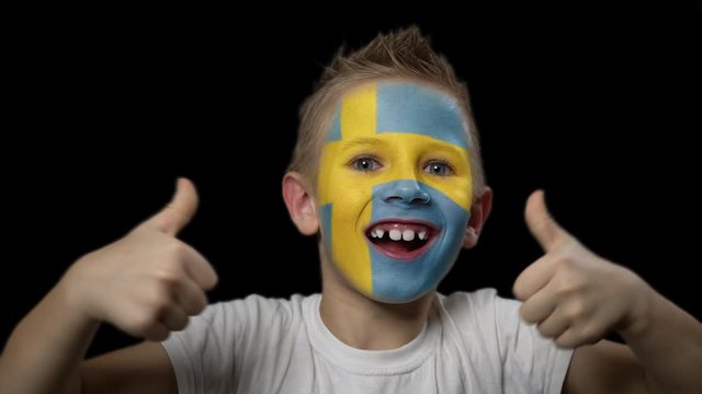 Happy boy rejoices victory of his favorite team of Sweden. A child with a face painted in national colors. Portrait of a happy young fan. Joyful emotions and gestures. Victory. Triumph.