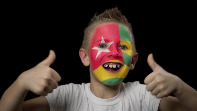 Happy boy rejoices victory of his favorite team of Togo. A child with a face painted in national colors. Portrait of a happy young fan. Joyful emotions and gestures. Victory. Triumph.