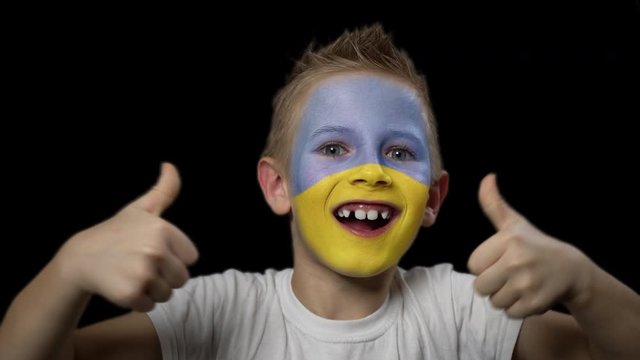 Happy boy rejoices victory of his favorite team of Ukraine. A child with a face painted in national colors. Portrait of a happy young fan. Joyful emotions and gestures. Victory. Triumph.