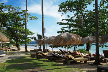 Arrangement and setting of tropical sunbathing daybeds with tourists facing the ocean