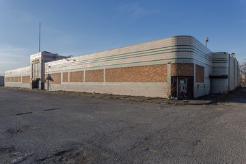 Large abandoned retail building with bricked over windows, weed filled sidewalks and rounded corners