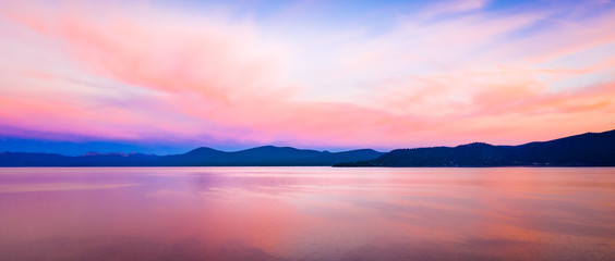 Wide background panorama of a brilliant colorful sky reflecting off water at sunset