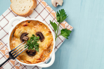 Casserole with chicken, mushrooms and cheese known in Russia as julienne in white bowl with herbs on a blue table, top view, flat lay, copy space