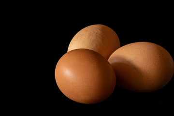 Three brown chicken eggs black background, close up. some eggs on black background. No people.