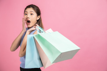 Asian pretty young woman sitting on pink  pastel background. She smiling and  happy shopping bags. she nice-looking lovely attractive shine She holding mobile.