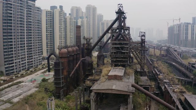 Slow pivot around abandoned steel mill plant metal structures in between living apartment blocks, Guangzhou, China, Aerial shot.