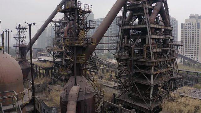Slow dolly in in between metal structures and machinery of an abandoned steel mill on a cloudy day, Guangzhou, China.