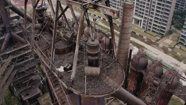 Slow pivot around the top of  abandoned steel plant metal structures with blast furnaces in between living apartment blocks, Guangzhou, China, Aerial shot.