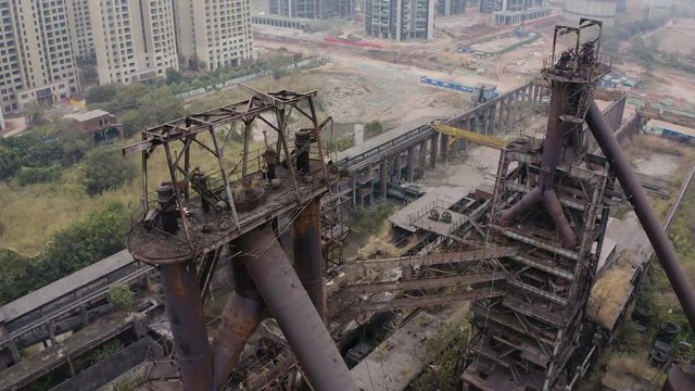 Slow pivot around the top of  abandoned steel plant metal structures with blast furnaces in between living apartment blocks, Guangzhou, China, Aerial shot.