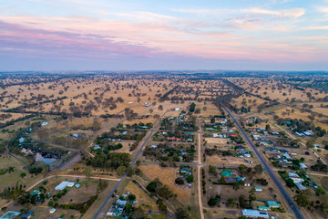 Aerial view of rural road passing through Australian countryside and small settlement at sunset