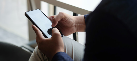 Cropped shot view of man hands holding smart phone with blank copy space screen for your text message or information content, female reading text message on cell telephone during in urban setting. 