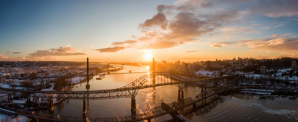 Fototapeta premium Aerial Panoramic View of the Modern City, Bridge and Fraser River during a colorful Sunset. Taken in New Westminster, Vancouver, British Columbia, Canada.
