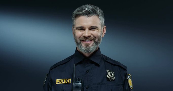 Portrait shot of the young Caucasian good looking and joyful policeman with gray hair smiling to the camera. Close up.