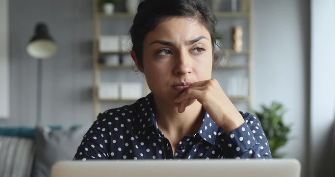 Thoughtful concerned indian woman working on computer thinking solving problem