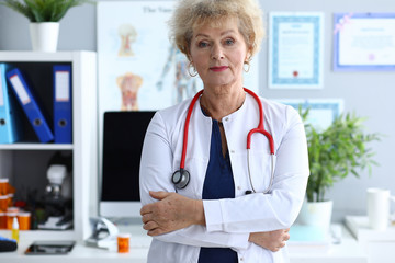 Portrait of successful professional doctor in medical gown standing at hospital office. Aged therapist smiling and looking at camera with calmness. Medicine and healthcare concept