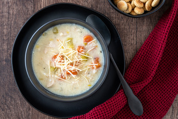 Greek lemon rice soup in a black bowl and black plate, black spoon and red napkin, rustic wood table, oyster crackers