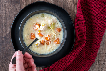 Greek lemon rice soup in a black bowl and black plate, woman’s hand with black spoon, red napkin