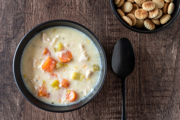 Greek lemon rice soup in a black bowl on a rustic wood table, black spoon, oyster crackers