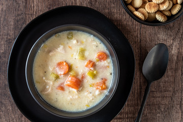 Greek lemon rice soup in a black bowl and black plate, black spoon, on a rustic wood table, oyster crackers
