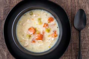 Greek lemon rice soup in a black bowl and black plate, black spoon, on a rustic wood table