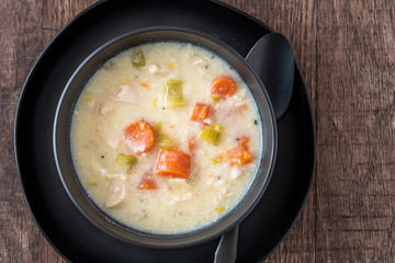 Greek lemon rice soup in a black bowl and black plate, black spoon, on a rustic wood table