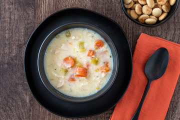 Greek lemon rice soup in a black bowl and black plate, black spoon on orange napkin, rustic wood table, oyster crackers