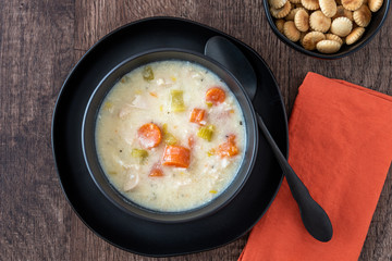 Greek lemon rice soup in a black bowl and black plate, black spoon and orange napkin, rustic wood table, oyster crackers