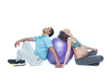Fototapeta na wymiar A young couple and their wife in the last months of pregnancy are sitting on a sports mat near the ball. Black man and white woman. The concept of a happy couple of different races preparing together