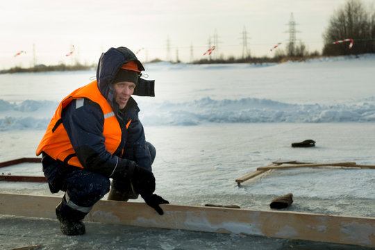 Worker in an orange helmet with a hood on his head