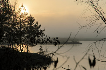 Landscape of a winter lake with tree branches in blur on the foreground and evening haze over the horizon, beautiful sunset