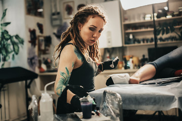 Fototapeta na wymiar Hipster woman with tattoos dreadlocks makes tattoo