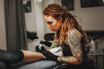 Fototapeta na wymiar girl with dreadlocks and tattoos stuffs tattoo leg