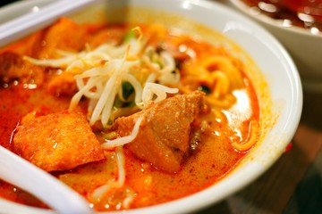Delicious bowl of curry laksa with noodles, tofu puffs, and chicken, served with a side drink.