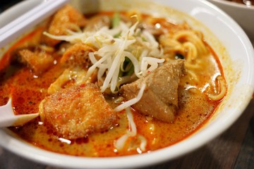 Delicious bowl of curry laksa with noodles, tofu puffs, and chicken, served with a side drink.