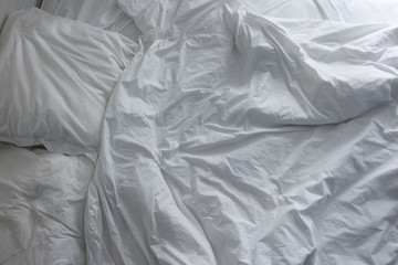 Untidy crumpled bed with white bedclothes.