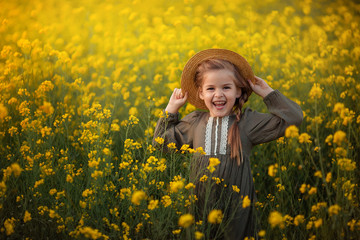 Fototapeta premium portrait of a cute beautiful girl with a pigtail in a straw boater. In the rays of the setting sun on a yellow rape field